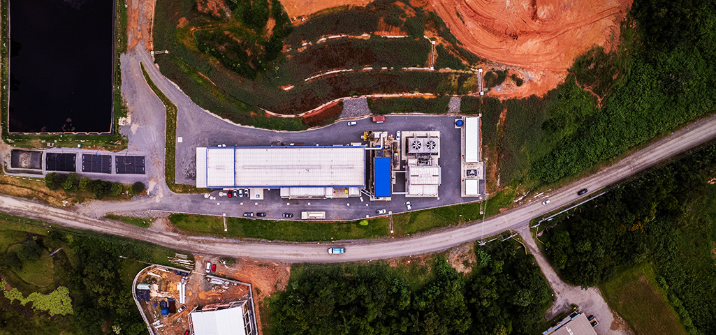 Imagem aérea de um estabelecimento industrial localizado próximo a uma rodovia, rodeado por áreas verdes e com infraestrutura moderna.