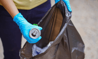 Pessoa recolhendo lixo usando luvas de proteção e uma sacola de lixo.
