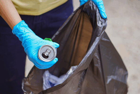 Pessoa recolhendo lixo usando luvas de proteção e uma sacola de lixo.