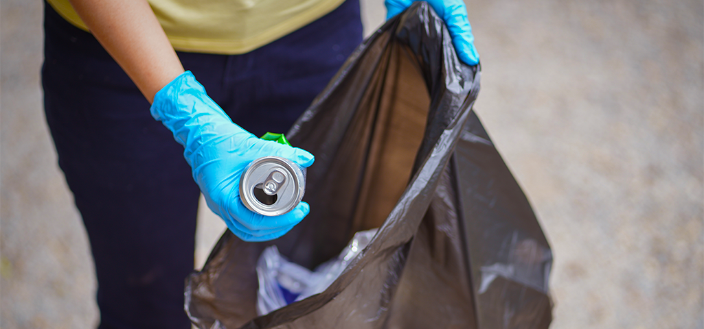 Pessoa recolhendo lixo usando luvas de proteção e uma sacola de lixo.