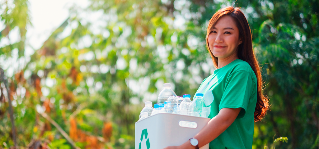 Mulher carregando caixa com materiais recicláveis.